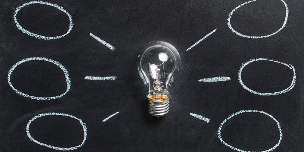 A lightbulb on a chalkboard with chalk lines coming out of it leading to bubbles for ideas