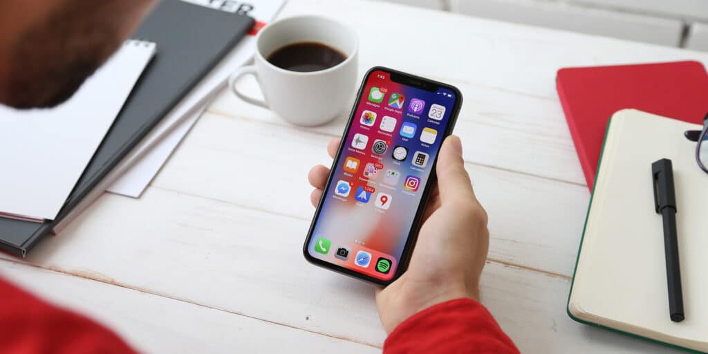 A person holding a cell phone next to a cup of coffee on an office work surface.