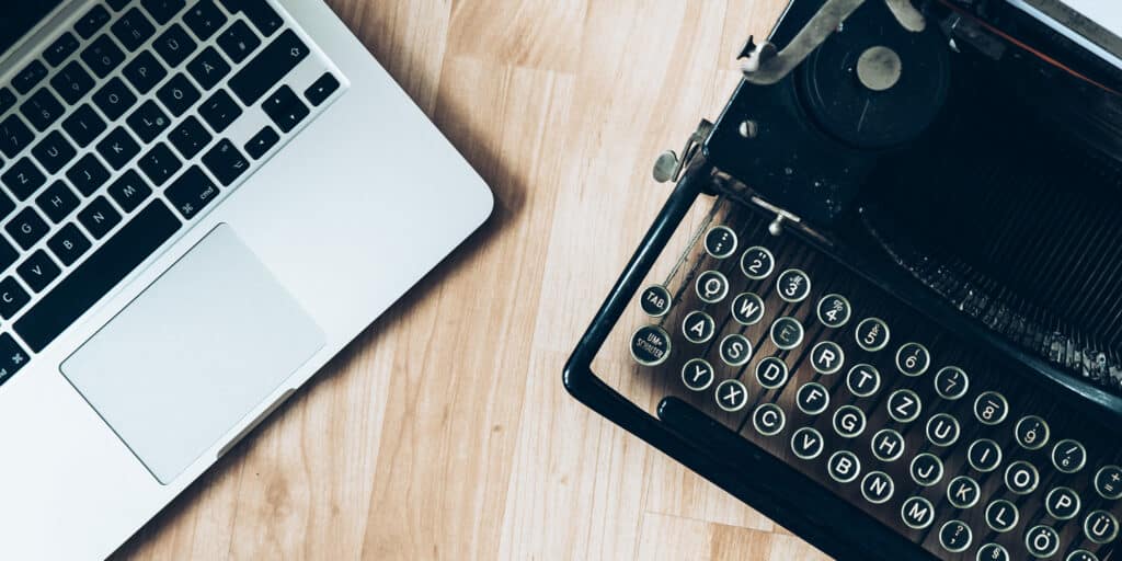 A laptop computer sitting next to a manual typewriter on top of a wooden table.