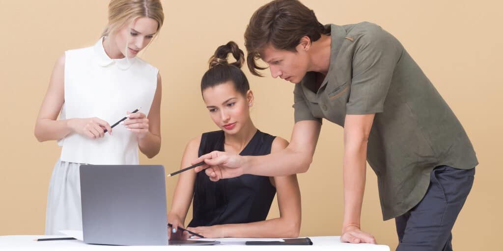 A man and two women looking at an open laptop.