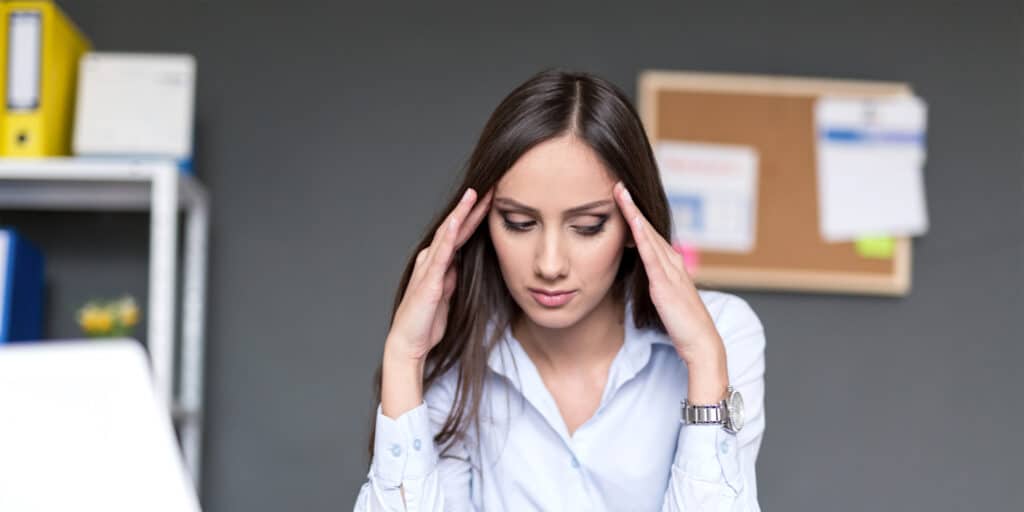 A stressed-out business woman sitting at a desk with her hands on her head.