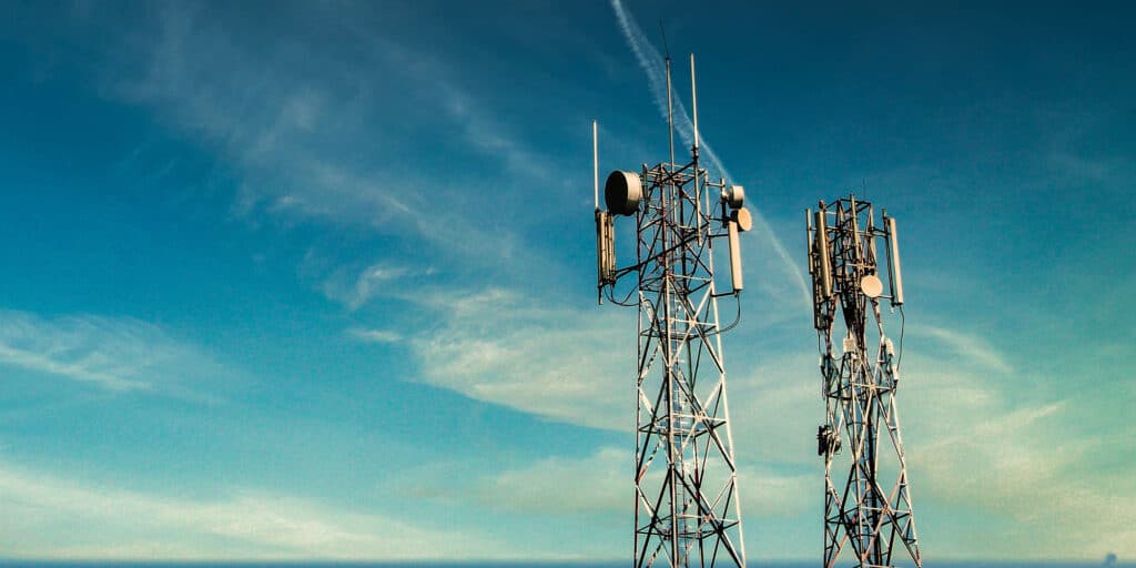 Two 5G cell towers standing next to each other against a cloudy blue sky.